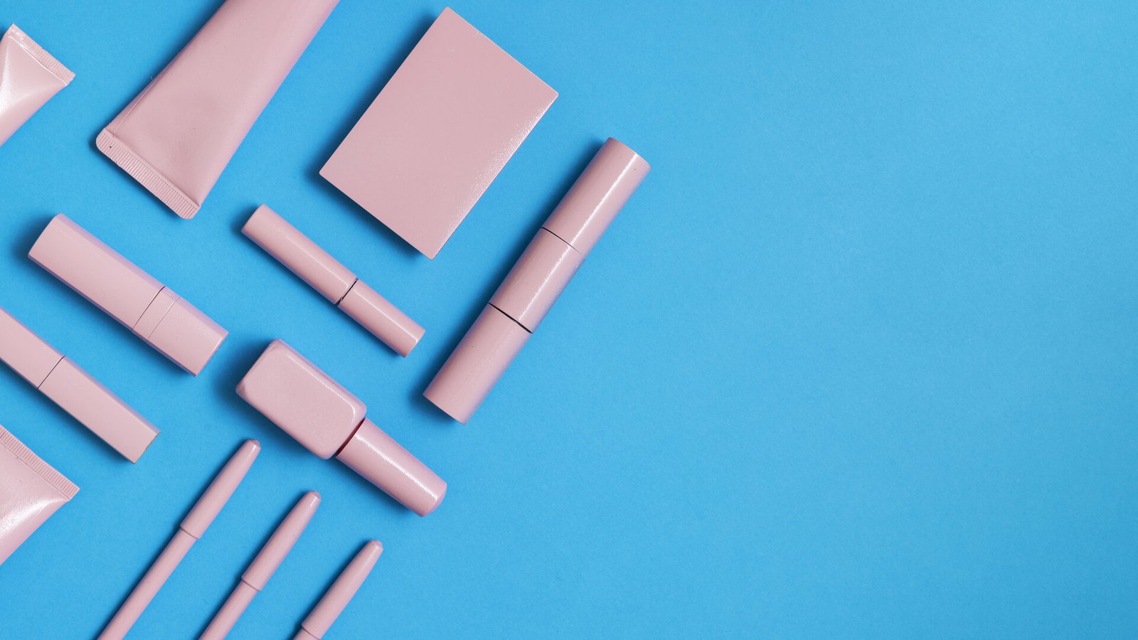 Des tubes de gloss et de rouge à lèvres rose pâle disposés sur un fond bleu.