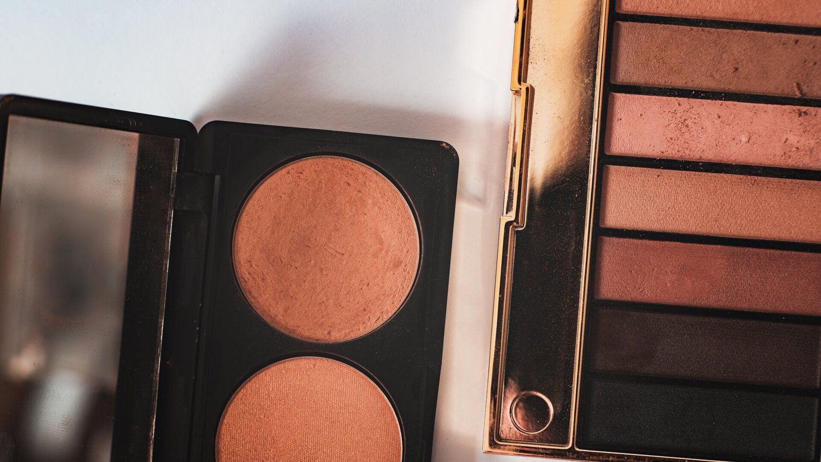 Un duo de fards couleur terracotta et une palette de tons bruns, posés sur une surface claire.