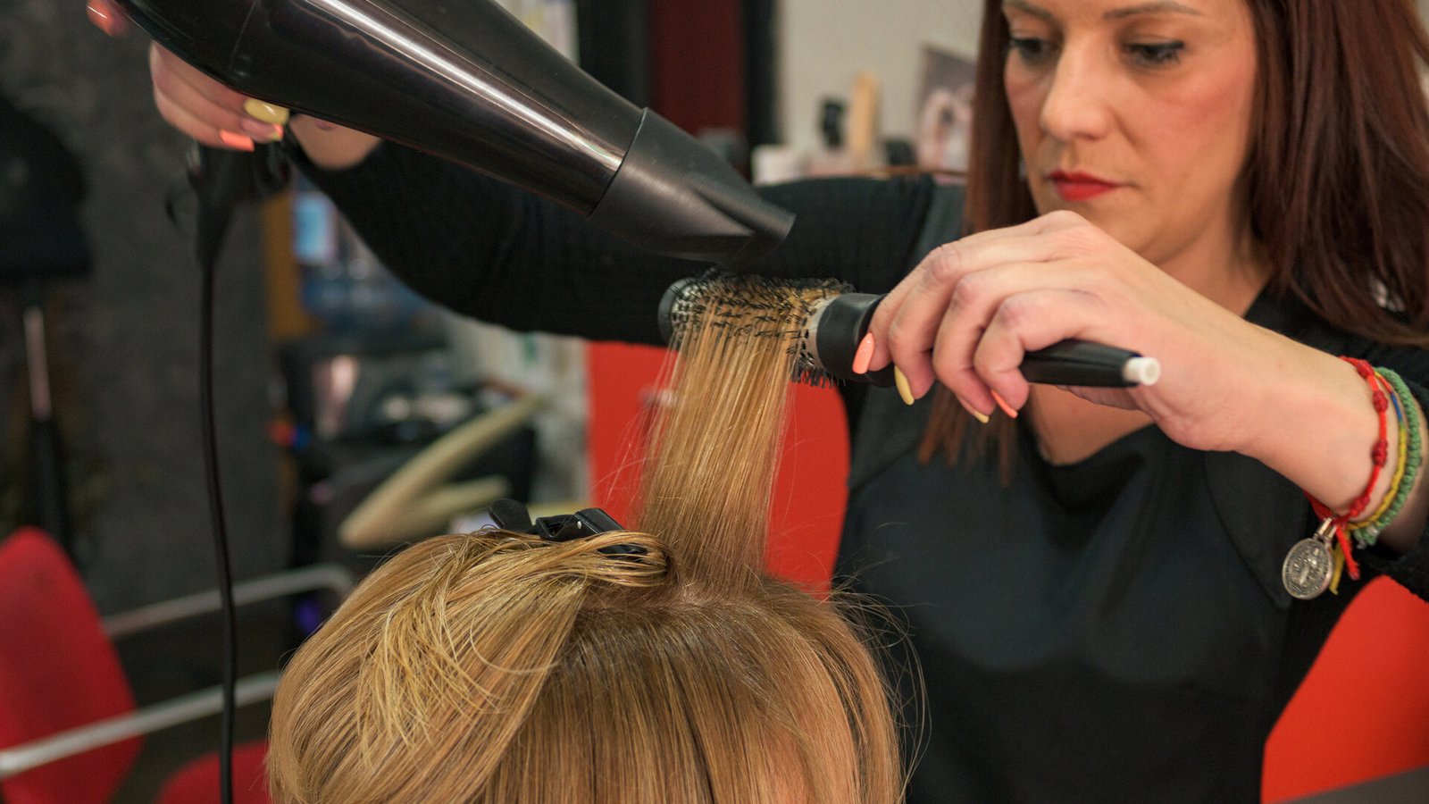 Une coiffeuse met en forme les cheveux d'une cliente avec un sèche-cheveux et une brosse ronde.