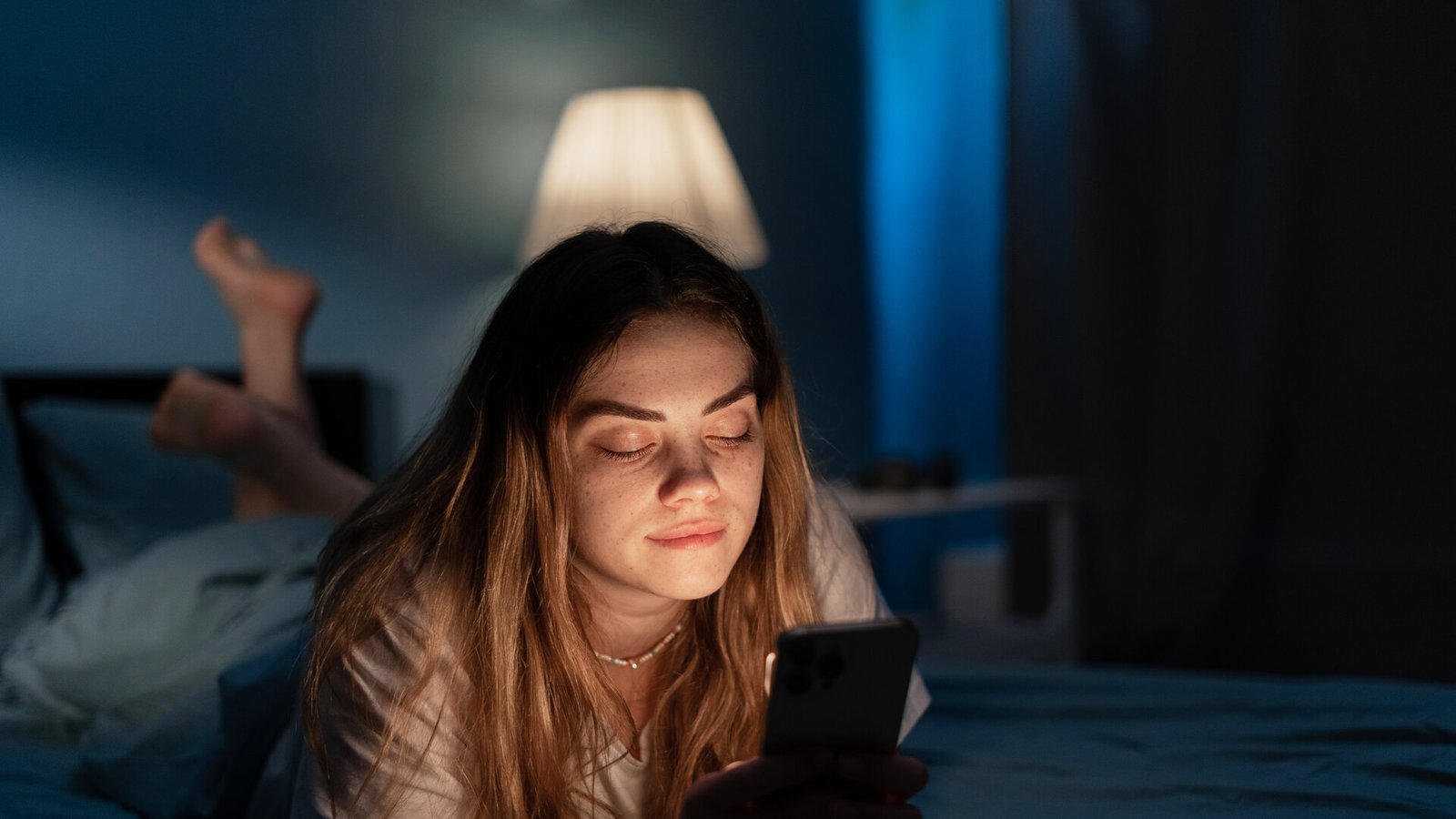 Une femme fatiguée, allongée dans son lit la nuit, fait défiler l'écran de son téléphone.