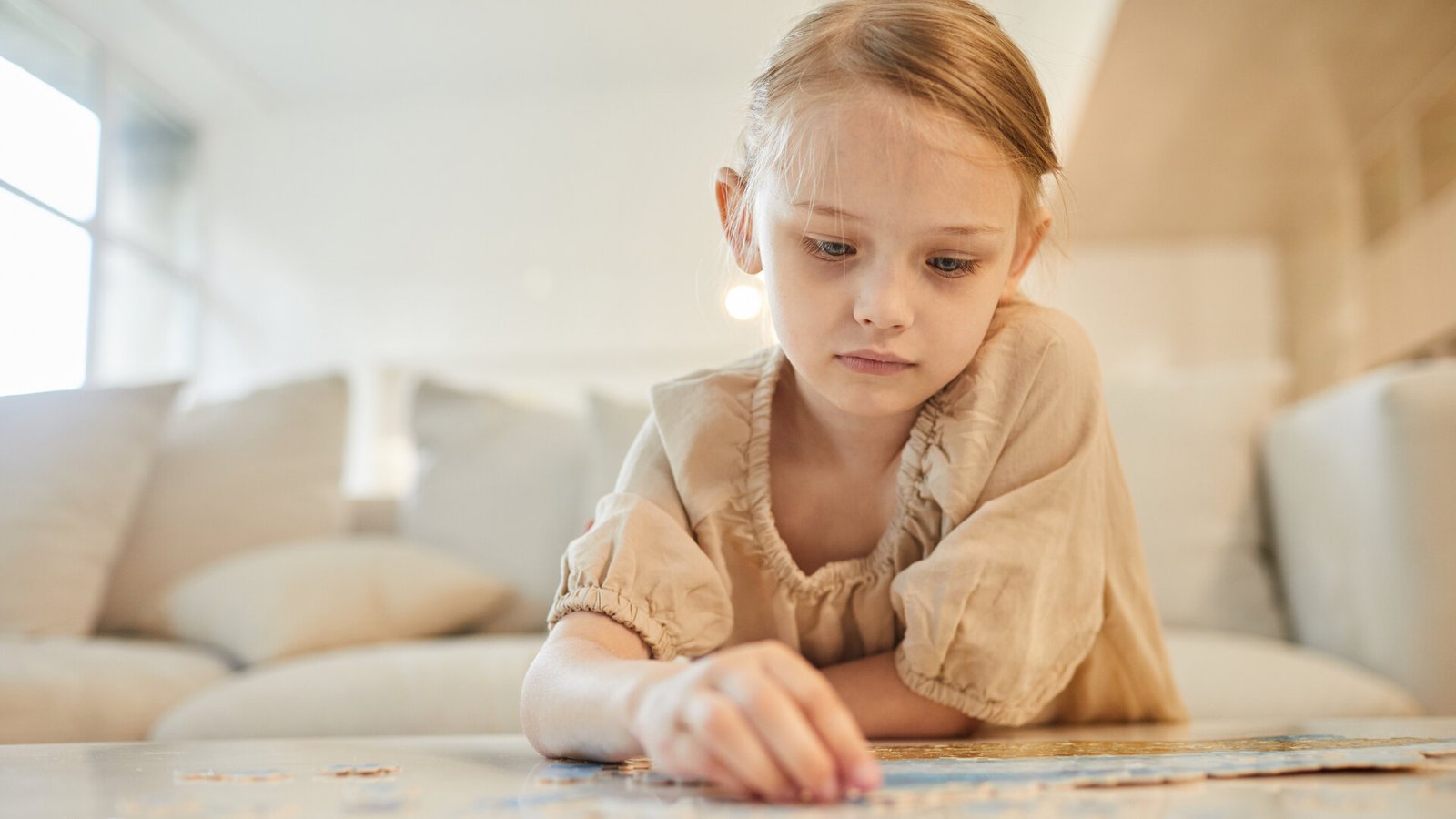 Une petite fille concentrée assemble un puzzle, seule à une table.