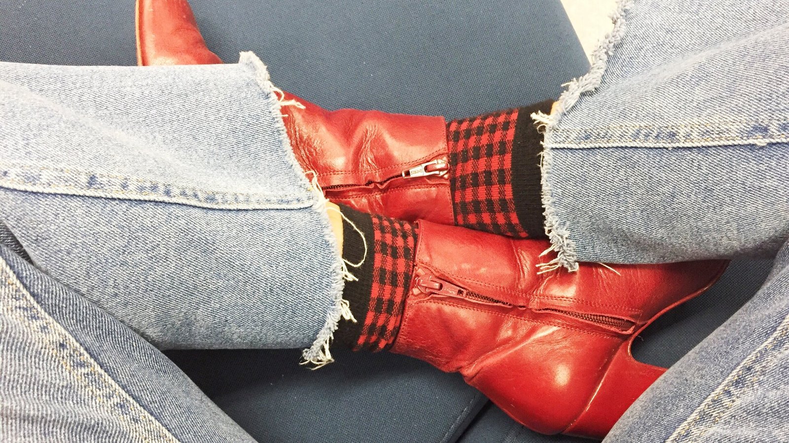 Gros plan sur des bottines rouges et l'ourlet effiloché d'un jean, là où le tissu rencontre la tige.