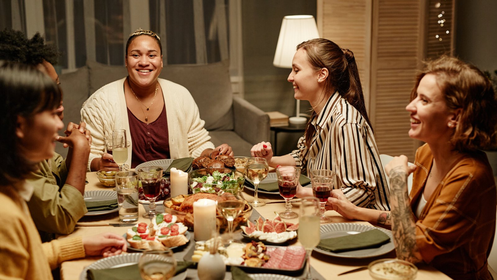 Un groupe d'amies rit autour d'une table de dîner garnie, verres à la main.
