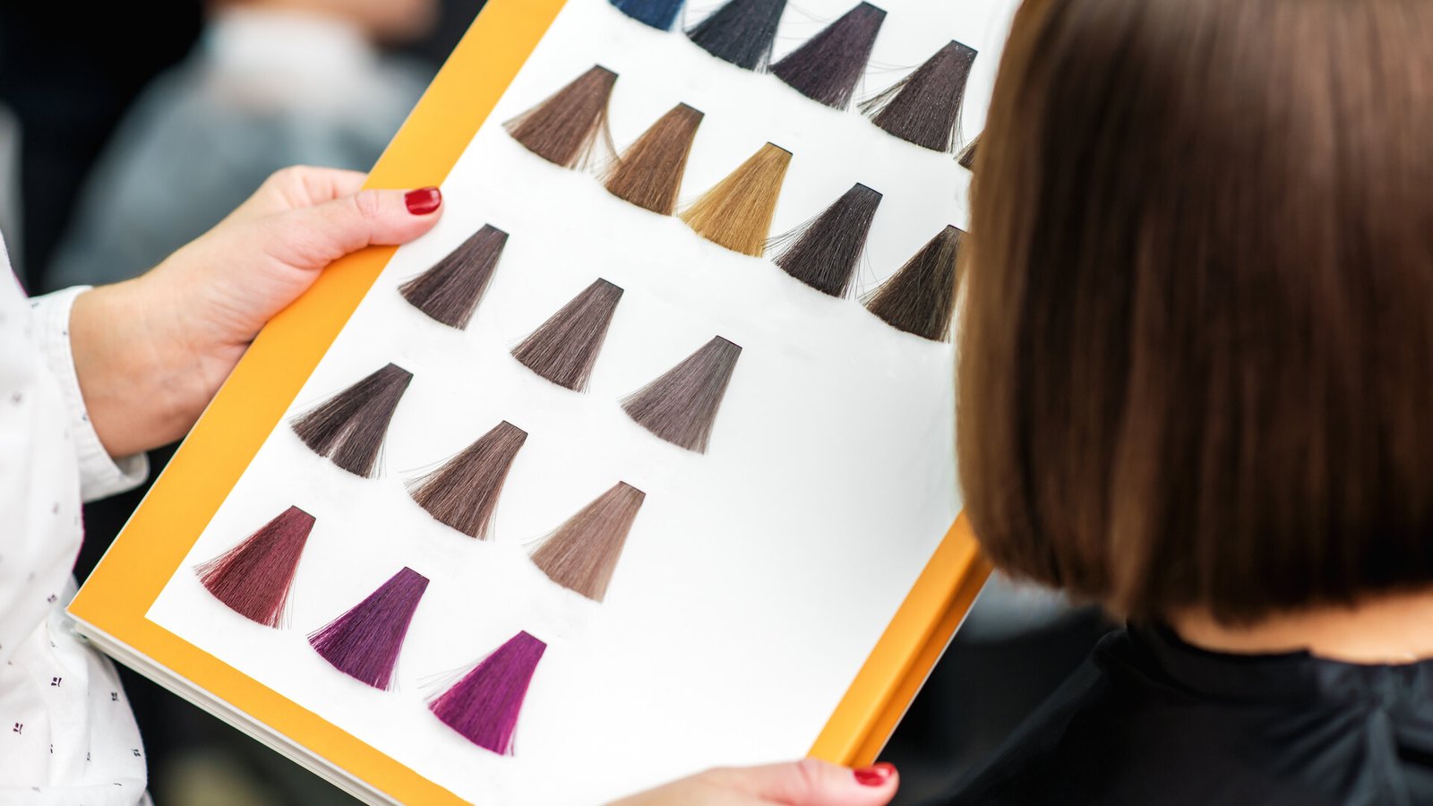 Une coiffeuse présente un nuancier de colorations à une cliente aux cheveux bruns coupés au carré.