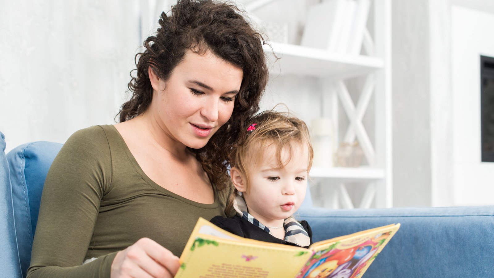 Une femme lit un livre illustré à un tout-petit assis contre elle sur un canapé